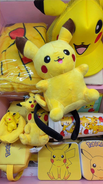 A yellow Pikachu inspired mystery gift box for kids featuring a large character plush toy, vibrant graphic baseball cap, fleece blanket, zippered pencil case, plush ears headband, and character water cup inside a pink surprise birthday package.